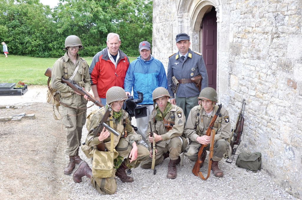 Filmakers Jim Karpeichik and Tim Gray (back row center) pose with some of the reenactors for their film, Eagles of Mercy, about two American medics who treated Allied and Gemran soldiers alike after D-Day in Normandy. They are standing outside the church they used as a medical station.
