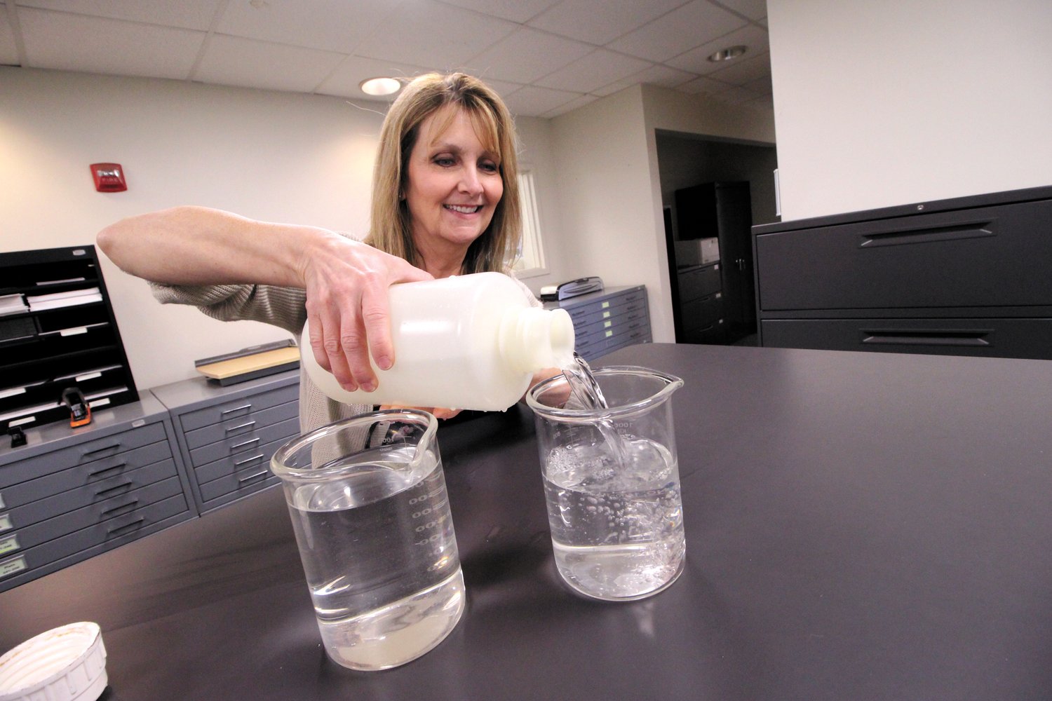 CAN YOU TELL THE DIFFERENCE? Look closely, but it’s unlikely you can identify tap water from effluent from Warwick’s wastewater treatment plant. Here Betty Anne Rogers , executive director of the Warwick Sewer Authority fills a beaker with effluent discharged into the Pawtuxet River. (Warwick Beacon photo)