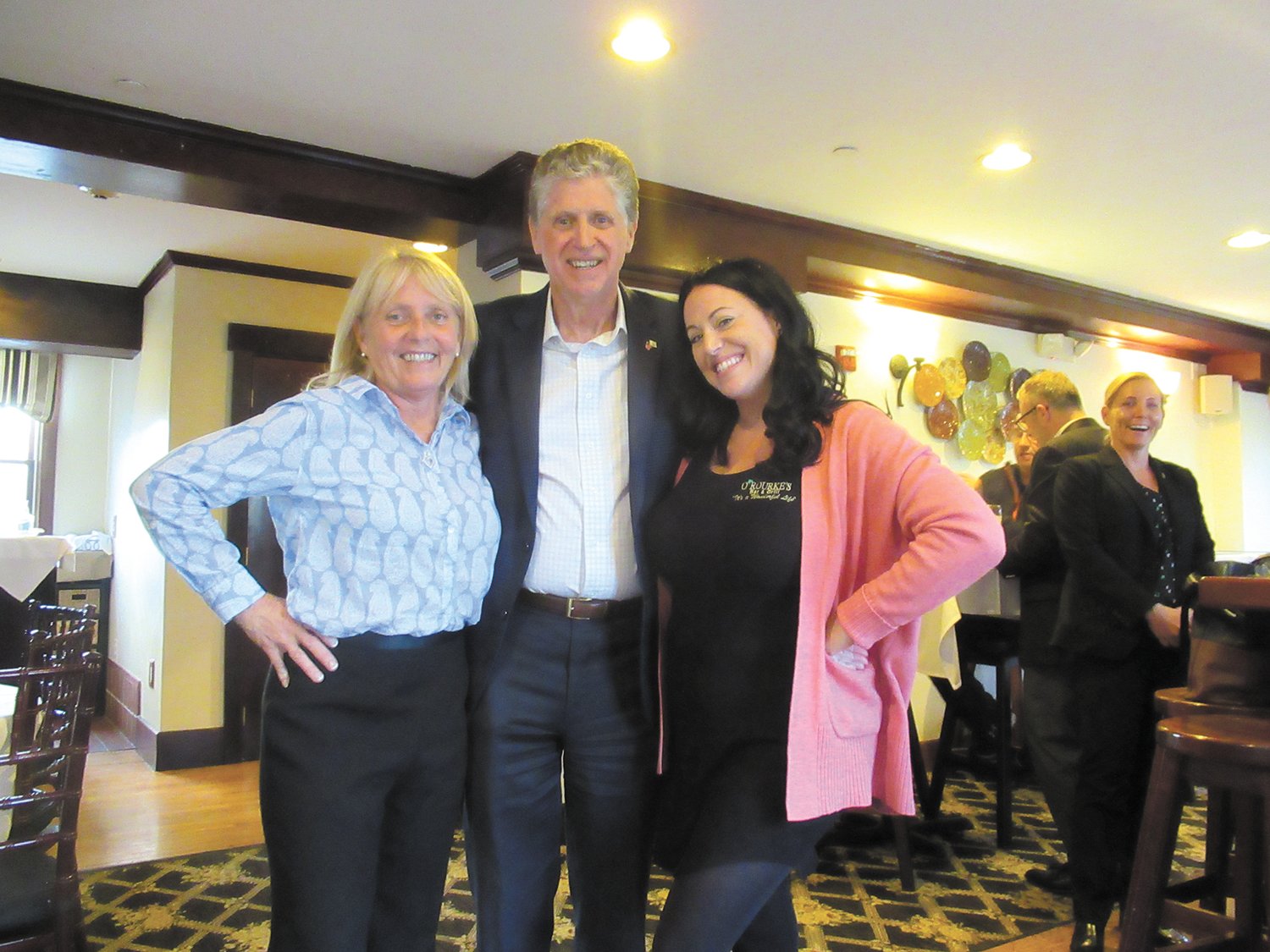 HAPPY HOSTS: Laurie O’Rourke (left), owner of O’Rourke’s Bar & Grill in Pawtucket Village and mixologist Amy Chaffee are all smiles as they welcome Gov. McKee.