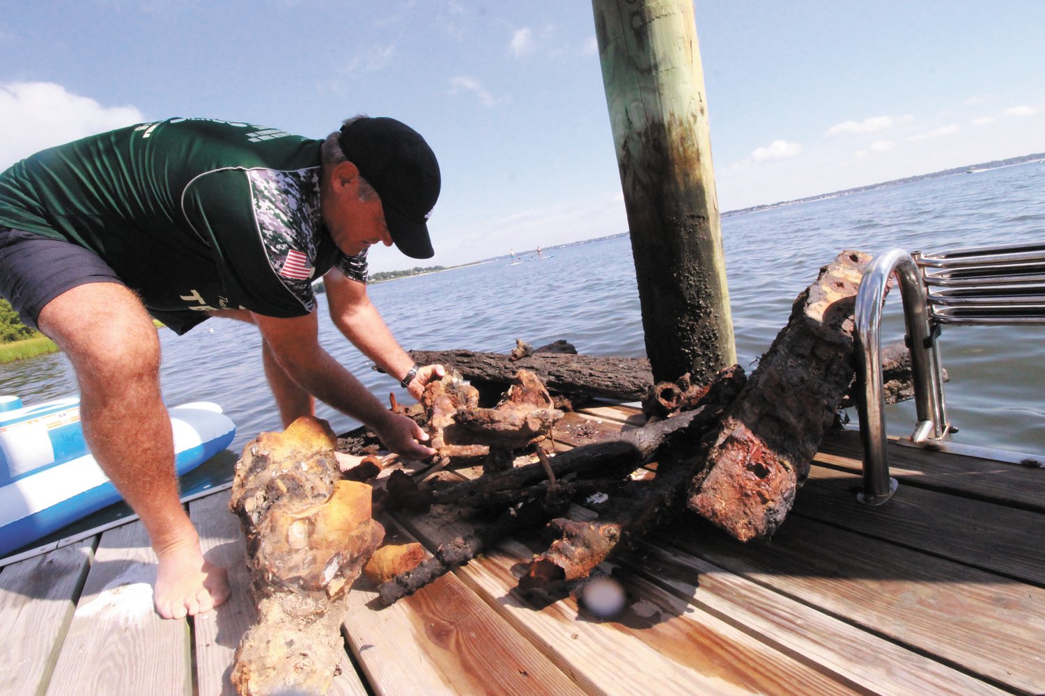 WHAT IS IT? Keith Strickland with some of the sunken debris recovered from the shallows in front of his home in Conimicut. He thinks the large chunk, which is metallic, could be the cleat off a ship. (Warwick Beacon photo)