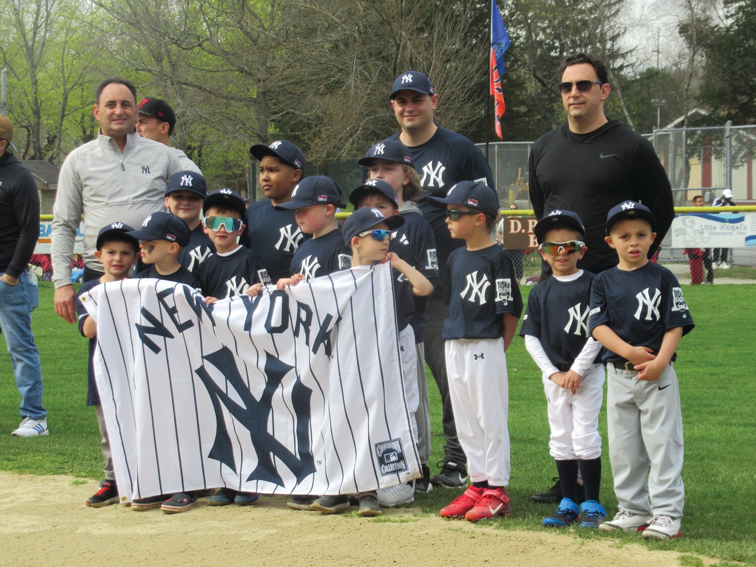 PINSTRIPE PACK: As they hold a special banner, the JLL’s Yankees, managed by Steve Mandarelli and Richard DelFino enjoy the excitement of Opening Day.
